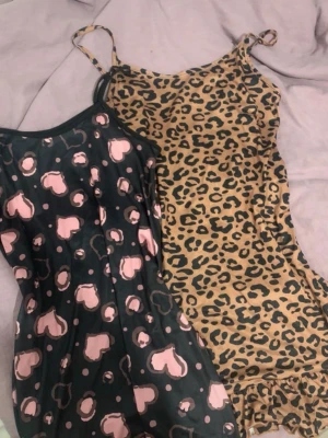 Två nattlinnen med mönster - Säljer två nattlinnen med tunna axelband. Ett är leopardmönstrat i brunt och svart, det andra är svart med rosa hjärtan. Båda har en figurnära passform och är perfekta för mysiga kvällar hemma.
