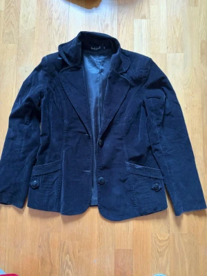 Svart manchesterkavaj från Elle Westend - Stilren svart kavaj i manchestertyg från Elle Westend. Klassisk modell med två knappar framtill, två fickor med lock och snyggt foder. Perfekt för dig som vill ha en tidlös och trendig look med lite extra struktur tack vare manchestertyget. (Stifles är mer som M/L)