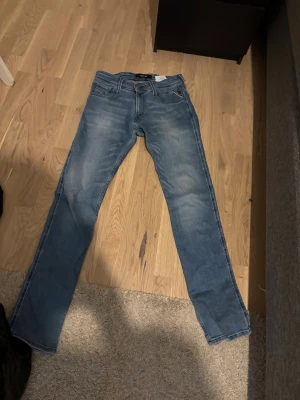 Blå slim fit jeans från Replay - Snygga blå slim fit jeans från Replay med klassisk femficksdesign och diskreta slitningar framtill. Jeansen har normal midja och raka ben, perfekta för en avslappnad men ändå stilren look. Tillverkade i mjuk denim för skön komfort.