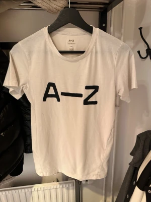 Vit t-shirt från A–Z med tryck - Snygg vit t-shirt från A–Z med svart tryck 'A–Z' på bröstet. Klassisk rund halsringning och korta ärmar. Tillverkad i mjukt bomullsmaterial som känns skönt mot huden. Perfekt för en avslappnad och stilren look.