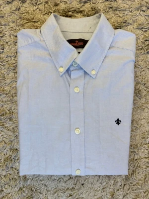 2 skjortor - Klassisk ljusblå skjorta från Morris med button-down krage och broderad logga på bröstet. Skjortan har långa ärmar, knappar framtill och är tillverkad i bomull. Perfekt för en stilren look.