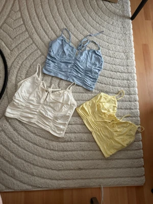 3 croppade linnetoppar i pastell - Säljer tre croppade linnetoppar i pastellfärger: ljusblå, vit och ljusgul. Alla har smala axelband, v-ringning och snygga rynkade detaljer framtill. Perfekta för sommaren och lätta att matcha med jeans eller kjol.nytt pris per st 250kr!