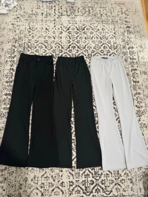 Tre par bootcut byxor i svart och vitt - Säljer tre par bootcut byxor, två svarta och ett vitt par. Alla har hög midja och utsvängda ben, perfekta för en trendig och avslappnad look. Materialet känns mjukt och stretchigt, vilket gör dem bekväma hela dagen.