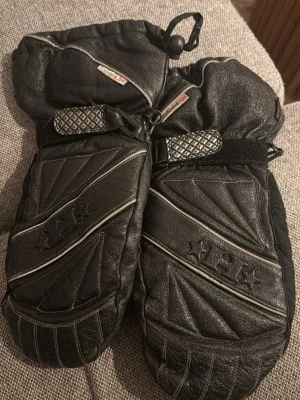 Svarta tumvantar från 3M Scotchlite - Svarta tumvantar från 3M Scotchlite med coola detaljer och reflexband. Vantarna är tillverkade i skinn och har justerbara band vid handleden för bättre passform. Perfekta för kalla vinterdagar när du vill hålla händerna varma och samtidigt se snygg ut.