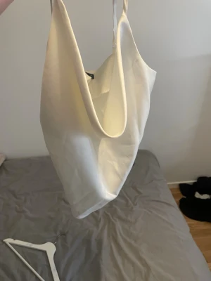 Vit linnetopp från Gina Tricot - Säljer en stilren vit linnetopp från Gina Tricot med tunna axelband och lös passform. Toppen har ett snyggt omlottliknande fall framtill och är tillverkad i ett lätt, svalt material som passar perfekt till sommaren.