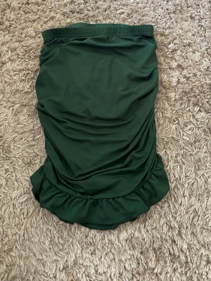 Grön volangkjol från SHEIN - Mörkgrön kortkjol från SHEIN med volangkant nedtill. Kjolen har en enkel, stilren design och är tillverkad i ett mjukt syntetmaterial med stretchig midja. Perfekt för dig som gillar trendiga och bekväma plagg.