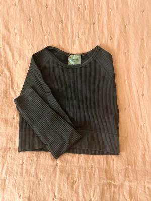 Svart ribbad croppad topp från Aimn - Snygg svart croppad topp från Aimn med lång ärm och ribbad struktur. Perfekt till jeans eller kjol för en trendig look. Enkel rund halsringning och mjukt material som sitter skönt på kroppen.