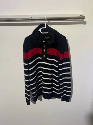 Randig stickad tröja med krage lauren Ralph lauren - Säljer en stickad tröja från Lauren Ralph Lauren. i marinblått med vita ränder och en röd rand över bröstet. Tröjan har hög krage, knappar framtill och långa ärmar. Perfekt för dig som gillar klassisk och sportig stil.