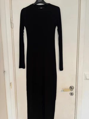 Svart långärmad långklänning - En stilren svart långklänning med lång ärm och rund halsringning. Klänningen är tillverkad i ett bekvämt material som är lätt att röra sig i. 