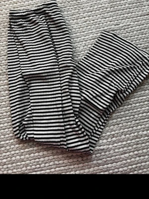 Randiga svartvita mjukisbyxor - Säljer ett par mjukisbyxor med svartvita horisontella ränder. Byxorna har resår i midjan och är gjorda i ett mjukt, stretchigt material som känns skönt mot huden. Perfekta för chill dagar hemma eller när du vill ha en avslappnad look.