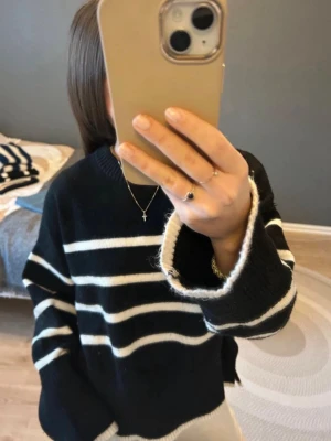 Svart stickad tröja med ränder Bershka - Säljer en svart stickad tröja från Bershka med vita horisontella ränder. Tröjan har rund halsringning, långa ärmar och ribbade muddar vid ärmslut och nederkant. Perfekt till jeans för en avslappnad look.