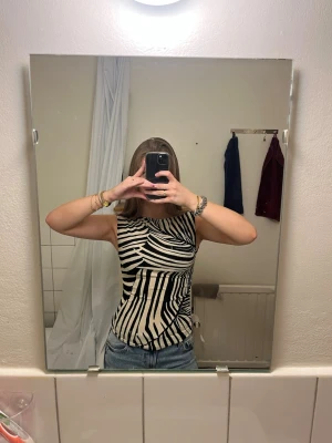 Zebramönstrad ärmlös linnetopp - Säljer en snygg zebramönstrad linnetopp i svart och vitt. Toppen är ärmlös och har en tight passform med rund halsringning. Perfekt att styla med jeans eller kjol för en trendig look.