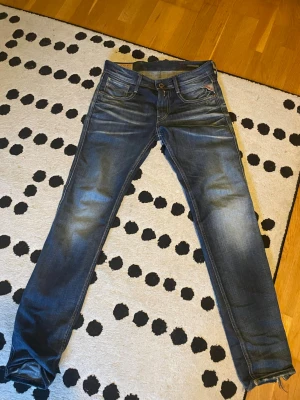 Blå slim fit jeans med slitningar - Säljer ett par blå slim fit jeans med snygga slitningar och tvättade detaljer. Jeansen har fem fickor, knappgylf och kontrastsömmar. Bakfickorna har dekorativa sömmar. Perfekta för en avslappnad och trendig look.