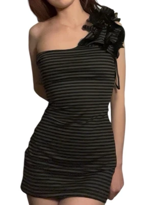 Svart och grå randig oneshoulderklänning - Snygg kortklänning med svarta och grå ränder i oneshoulder-modell. Klänningen har en stor volangdetalj på axeln som ger extra attityd. Tight passform och kort längd, perfekt för dig som vill sticka ut. Materialet känns mjukt och följsamt.