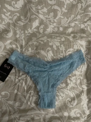 Blå spetsstring Hunkemöller - Söt ljusblå stringtrosa från Hunkemöller transparent spets med mjuka leopardmönster Trosan har dekorativ spetskant runtom och en liten rosett framtill. Prislappen sitter kvar 