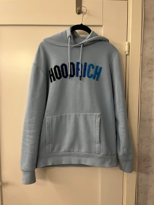 Ljusblå hoodie från Hoodrich S - Snygg ljusblå hoodie från Hoodrich i storlek S. Tröjan har broderad logga i svart, mörkblå och blå på bröstet, snörning i huvan och en stor magficka. Mjuk insida och klassisk passform. Snygg hoddie överlag, den har använts en del men är i väldigt bra skick ändå. Den har däremot två små röda färgfläckar som ej går bort men annars är allt som det ska. Hör av er om ni har frågor!