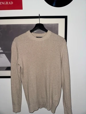Beige J.Lindberg tröja - Säljer en stilren beige ribbstickad tröja med rund hals och långa ärmar. Tröjan har en enkel och clean design som passar perfekt till olika outfits. Materialet känns mjukt och bekvämt, och den ribbade strukturen ger en snygg detalj.