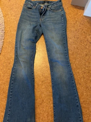 Blå bootcut jeans vero moda  - Säljer ett par klassiska blå bootcut jeans med fem fickor och normalhög midja. Jeansen har en snygg tvätt och stängs med knapp och dragkedja. Perfekta till sneakers eller boots för en avslappnad look. Jensen är från vero moda 