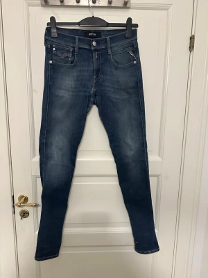 Blå slim fit jeans från Replay - Säljer ett par blå slim fit jeans från Replay med snygg tvättad look och klassiska fem fickor. Jeansen har en smal passform och är tillverkade i mjukt denimtyg med stretch för extra komfort. Perfekta för en avslappnad och trendig stil. Storlek 28/32