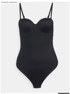 Svart basic body med tunna band - En stilren svart body med tunna, justerbara axelband och formpressade kupor. Bodyn har en slät och enkel design utan synliga sömmar, vilket ger en clean look. Perfekt att bära under kläder eller som ett statement-plagg. Materialet är  stretchigt och mjukt. Banden går att ta av