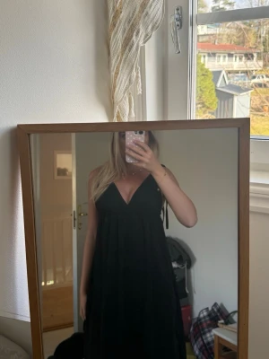 Svart långklänning med knytaxelband - Svart långklänning med djup v-ringning och knytbara axelband. Klänningen har en luftig passform.