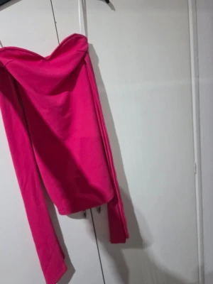 Axelbandslös rosa kortklänning - Trendig axelbandslös kortklänning i stark rosa färg. Klänningen har en figurnära passform och är tillverkad i ett mjukt material som ger en snygg siluett. Perfekt för dig som vill sticka ut och känna dig extra snygg.