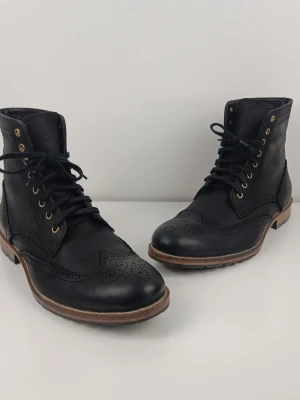 Human Scales Handgjorda Brogue Läderkängor Svarta EU44Svarta brogue stövletter i läder - Snygga svarta stövletter i äkta läder med klassiska broguedetaljer och snörning framtill. Skorna har robust sula i brunt och svarta skosnören samt mässingsfärgade öljetter. Perfekta för dig som gillar en stilren och tidlös look.