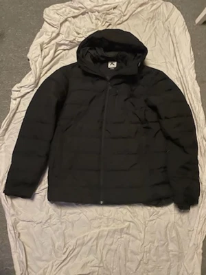 Svart pufferjacka med huva - Säljer en svart pufferjacka från Mountain Warehouse med huva och dragkedja framtill. Jackan har quiltad design och är vadderad för extra värme. Perfekt för kalla vinterdagar och har en stilren look som passar till det mesta.