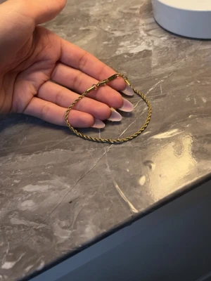 Guldfärgat armband i rostfritt stål - Snyggt guldfärgat armband i rostfritt stål med tvinnad kedja. Lätt att matcha med andra smycken och har en enkel men stilren design. Märkt med 'S.steel' på låset. Perfekt accessoar för dig som gillar minimalistiska detaljer.