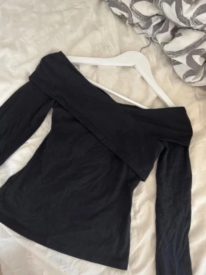 Svart offshoulder topp från H&M - Trendig svart offshoulder topp från H&M i stretchigt material. Toppen har långa ärmar och en bred kant som vilar snyggt över axlarna. Perfekt för dig som vill ha en stilren och enkel look med en twist. Litet hål där lappen suttit (bild 2)