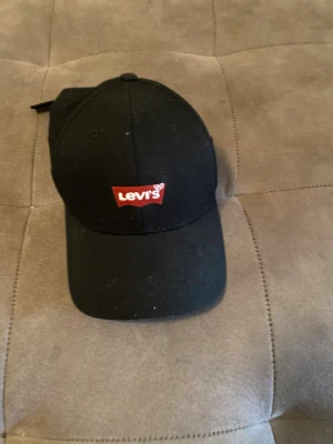 Svart keps från Levi's med logga - Snygg svart keps från Levi's med den klassiska röda loggan framtill. Kepsen har böjd skärm och justerbar rem baktill. Tillverkad i bomullstyg som ger en clean och stilren look.