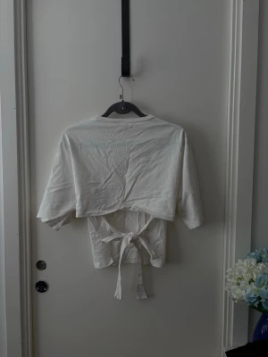 Vit croppad topp med knytband - Säljer en vit croppad topp med knytband i midjan och korta ärmar. Toppen har enkel design och är tillverkad i mjukt bomullsmaterial. Perfekt för dig som gillar en clean och stilren look.