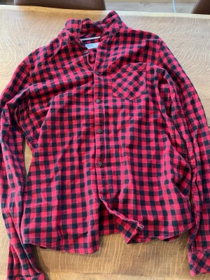 Röd och svart rutig skjorta  - Klassisk röd och svart rutig skjorta från Solid med lång ärm och bröstficka. Skjortan har knappar framtill och är tillverkad i mjuk bomull. Perfekt för en avslappnad och trendig look.