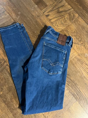 Blå Replay Hyperflex jeans - Riktigt Snygga blå jeans från Replay anbass Hyperflex med klassisk femficksdesign och kontrastsömmar. Jeansen har en skinnpatch med logga bak i midjan och är tillverkade i stretchigt denim för extra komfort. Perfekta för en avslappnad och trendig look.