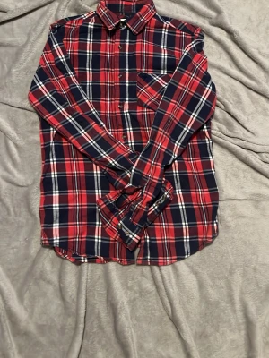 Röd och blå rutig skjorta - Klassisk rutig skjorta i rött, blått och vitt med lång ärm och knappar framtill. Skjortan har en bröstficka och mjukt material som känns skönt mot huden. Perfekt för en avslappnad och stilren look.