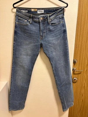 Ljus Blå jeans från Jack & Jones - Klassiska blå jeans från Jack & Jones med fem fickor och raka ben. Jeansen har en normalhög midja och är tillverkade i bomull med en lätt tvättad finish. Perfekta för en avslappnad och stilren look.