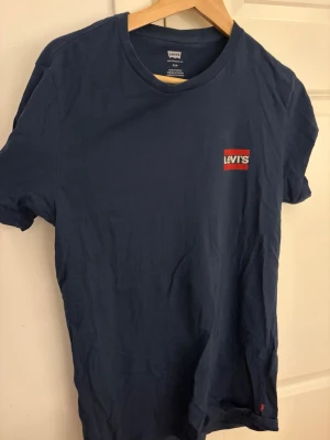 Mörkblå Levi's t-shirt med logga - Snygg mörkblå t-shirt från Levi's med klassisk röd och vit logga på bröstet. T-shirten har rund halsringning och korta ärmar. Tillverkad i mjuk bomull för en skön känsla. Perfekt till jeans eller shorts.