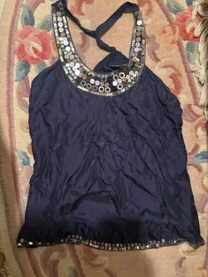 Mörkblå paljettprydd linnetopp - Snygg mörkblå linnetopp med halterneck och glittriga paljettdetaljer längs ringningen och nederkanten. Perfekt för dig som vill sticka ut lite extra. Tunn och luftig känsla.