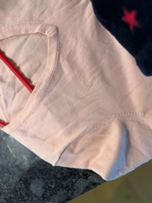 Ljusrosa stickad tröja Tommy Hilfiger - Snygg ljusrosa stickad tröja från Tommy Hilfiger med V-ringning och diskret logga broderad på bröstet. Tröjan har långa ärmar och ribbade muddar vid hals, ärmslut och nederkant. Perfekt för en stilren och avslappnad look. En liten flekt som kan tvättas bort.