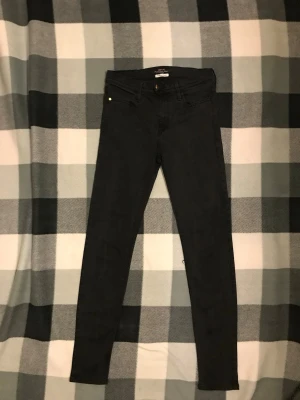 Svarta skinny jeans från Replay - Säljer ett par svarta skinny jeans från Replay med klassisk femficksdesign och läderpatch bak på linningen. Jeansen har smal passform och är tillverkade i stretchigt material som ger en bekväm känsla. Perfekta för dig som gillar en stilren look.