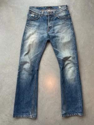 Nudie Jeans Regular Ralf - Säljer ett par klassiska blå jeans från Nudie Jeans med rak passform och snyggt slitna detaljer. Jeansen har fem fickor, knappgylf och kontrastsömmar. Tillverkade i bomull med en autentisk tvättad look och ljusa partier på lår och knän. Storlek 30w 32l. 