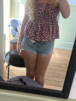 Ljusblå denimshorts med fransar - Säljer ett par ljusblå denimshorts med råa, fransiga kanter och låg midja. Shortsen har klassisk femficksdesign och knappar framtill. Perfekta för varma dagar och ger en avslappnad vibe.