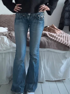 Blå bootcut jeans från True Religion - Säljer ett par blå bootcut jeans från True Religion. Jeansen har låg midja, dekorativa fickor bak och är utsvängda. 