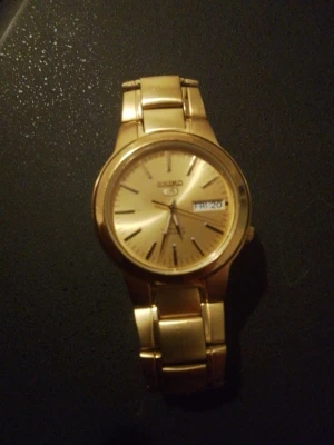 Guldfärgad Seiko armbandsur - Säljer en guldfärgad Seiko armbandsur med metallänk och rund urtavla. Klockan har dag- och datumvisning och en stilren, klassisk design. Perfekt accessoar för dig som gillar tidlösa detaljer och snygg finish.