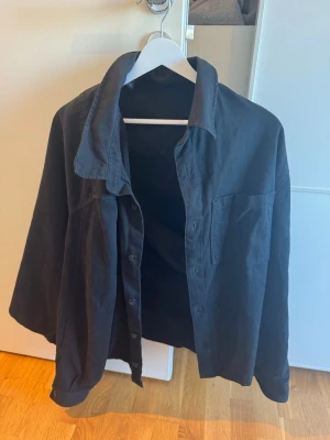 Svart skjorta från H&M i bomull XXL - Säljer en svart skjorta från H&M i storlek XXL. Skjortan är tillverkad i mjuk bomull, har klassisk krage, bröstficka och knäppning framtill. Perfekt för en avslappnad och stilren look.