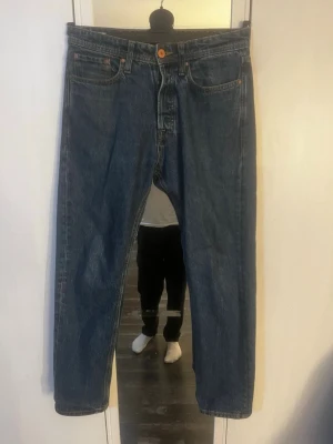 Blå raka jeans från Jack & Jones - Säljer ett par klassiska blå jeans från Jack & Jones i modellen relaxed/chris och fem fickor. Jeansen har en snygg mörk tvätt, orange sömmar och läderpatch med logga bak i midjan. Tillverkade i slitstark denim, perfekta till vardagslooken. Hör av er vid frågor! W29 L32