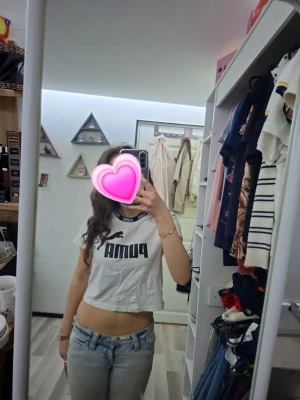 Vit croppad PUMA t-shirt - Säljer en vit croppad t-shirt från PUMA med svart logga och text framtill. T-shirten har rund halsringning med svart kant och korta ärmar. Perfekt för en sportig och avslappnad stil. 