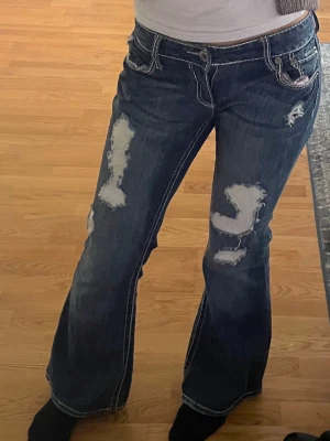 Blå slitna bootcut jeans - Säljer ett par mörkblå bootcut jeans med slitningar. Storlek S från tinlesell. Använda fåtal gånger