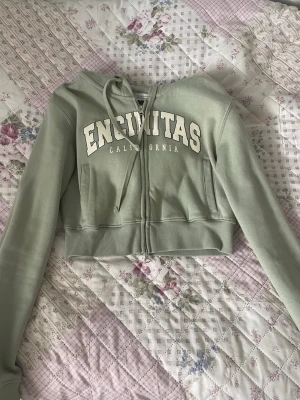 Grön cropped zip-tröja - Säljer min mint gröna korta zip-tröja med tryck från Bershka, använd en gång. Tröjan har två dragkedjor, är väldigt mjuk och varm. 