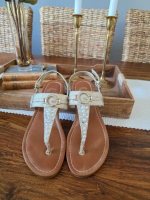 Guldiga sandaler från Guess - Snygga guldiga sandaler från Guess. Perfekta för sommaren och ger en lyxig touch till din outfit. Strl 37 🌿